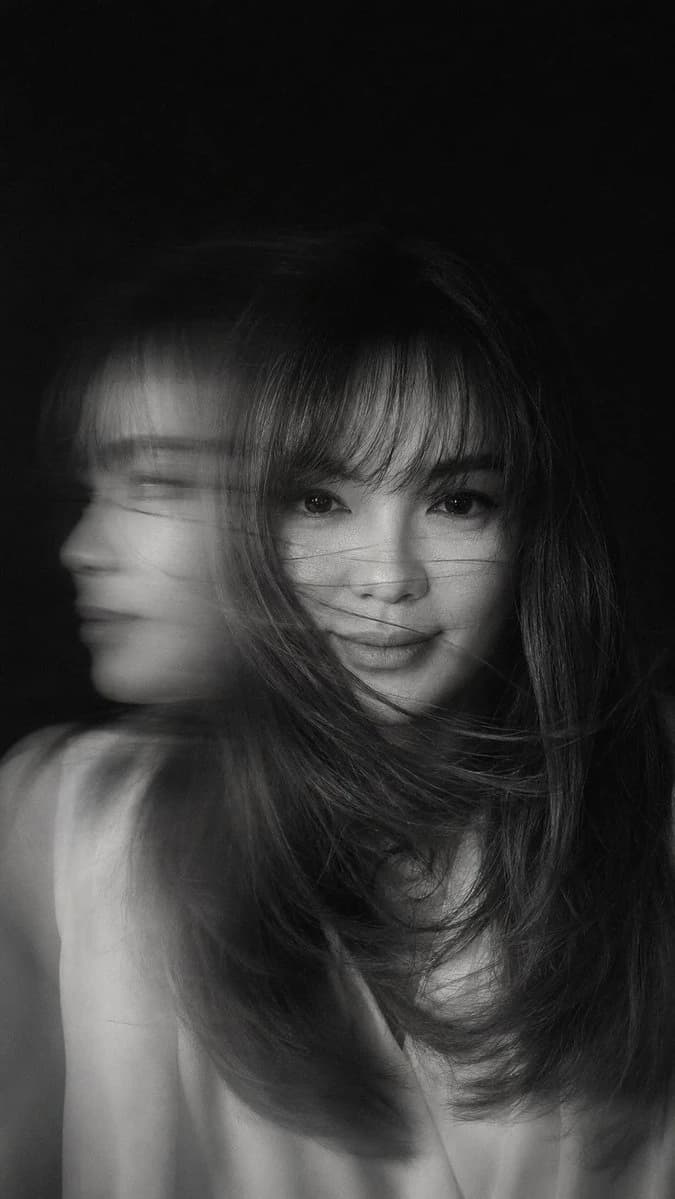 A hyper-realistic black-and-white portrait captures a woman in mid-motion, her face partially obscured by flowing hair and dynamic light streaks
