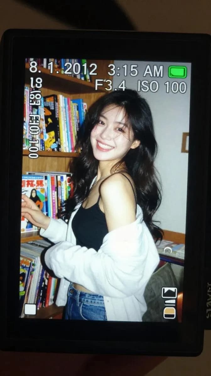 A close-up of a digital camera screen displays a candid photograph of a young woman laughing beside a shelf filled with colorful comic books