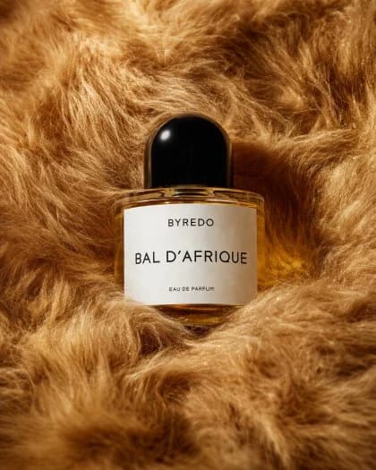 A close-up of a clear oval perfume bottle filled with amber liquid, nestled in rich golden faux fur, showcasing a minimalist design and elegant label