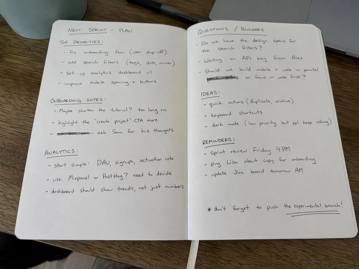 An open notebook with casual handwritten notes in black ink lies flat on a wooden desk, illuminated by natural daylight
