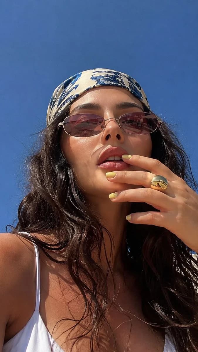 A low-angle summer macro selfie of a woman in sunlight, with bright outdoor color, close facial detail, and relaxed framing